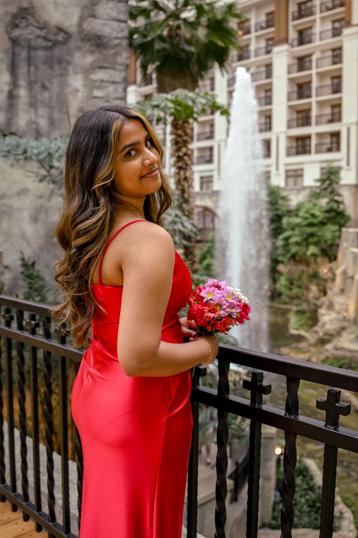 Portrait in a red dress holding a pink bouquet beside a stone courtyard
