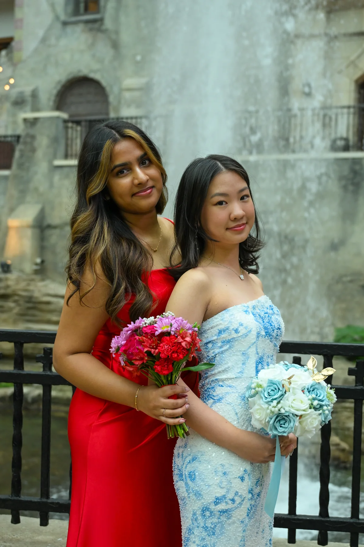 Two people holding bouquets in red and pale blue formal dresses