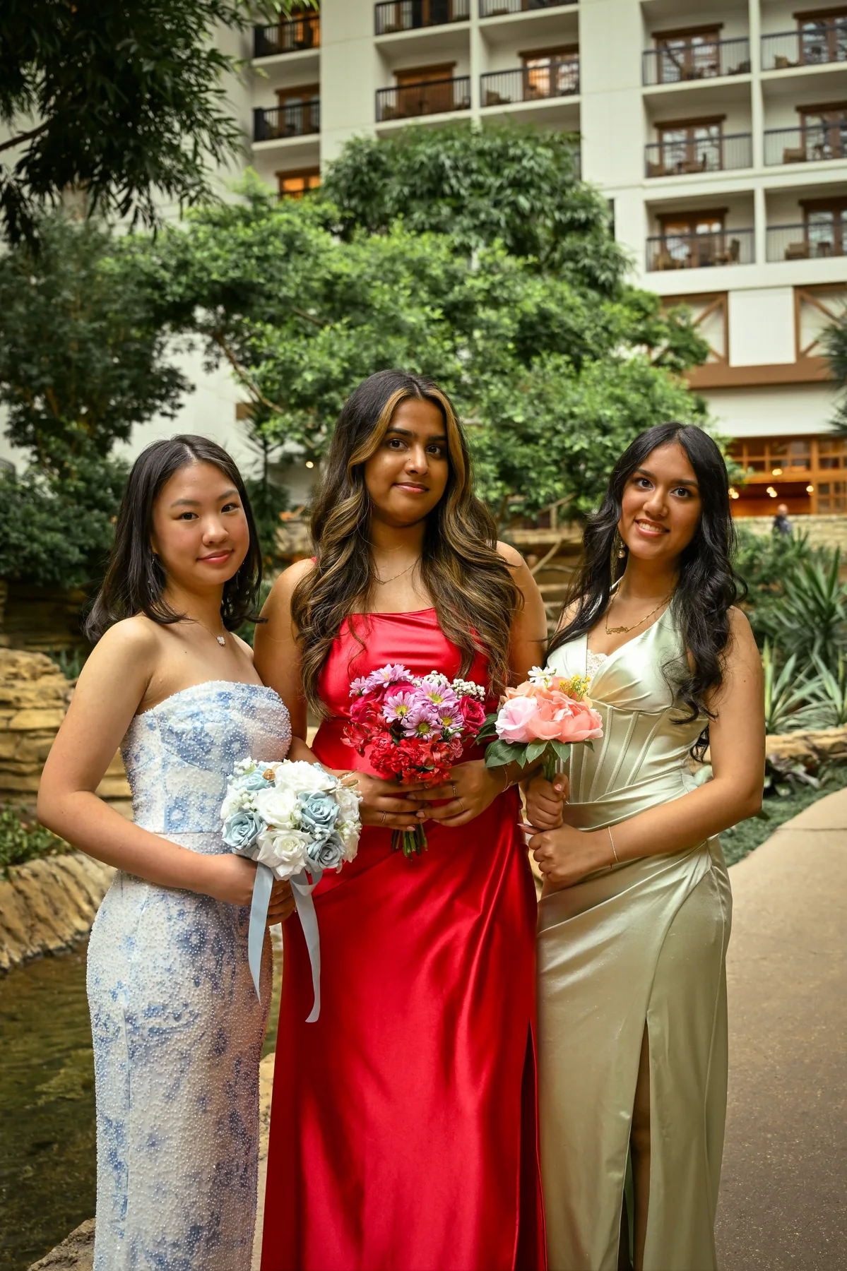 Three people holding bouquets in a sunlit courtyard