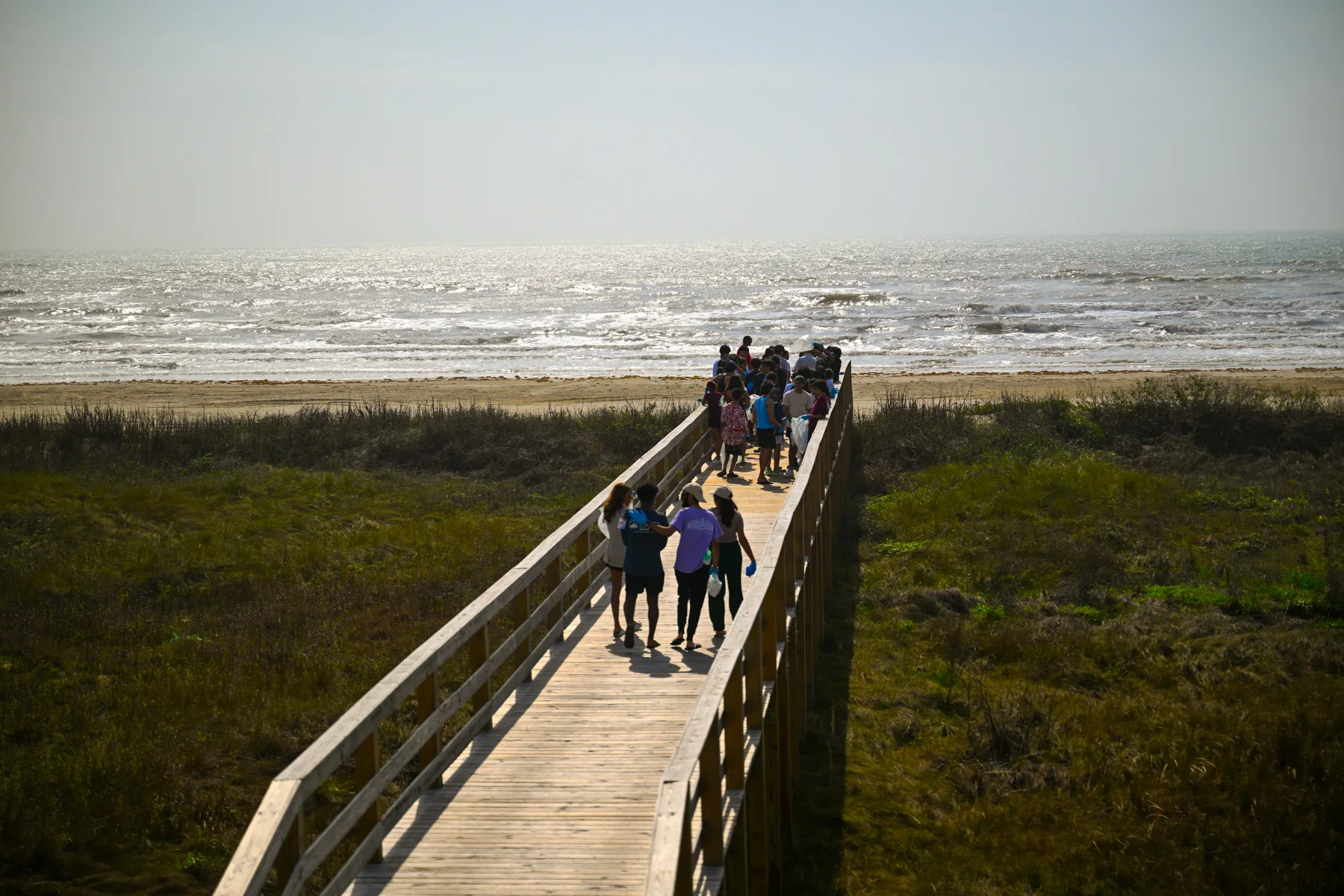 People walking down a wooden boardwalk toward the sea