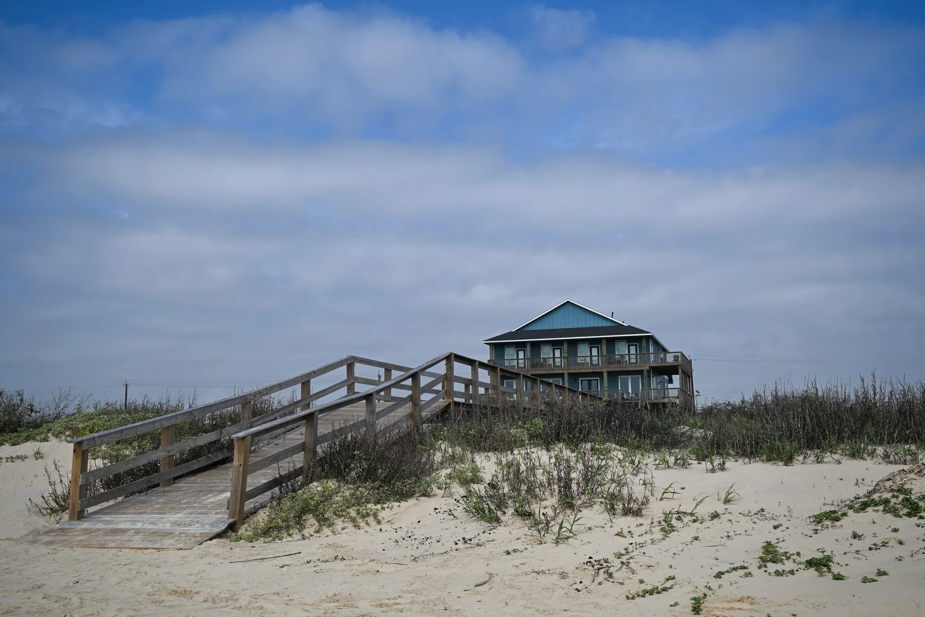 A weathered beach pavilion beyond white sand dunes