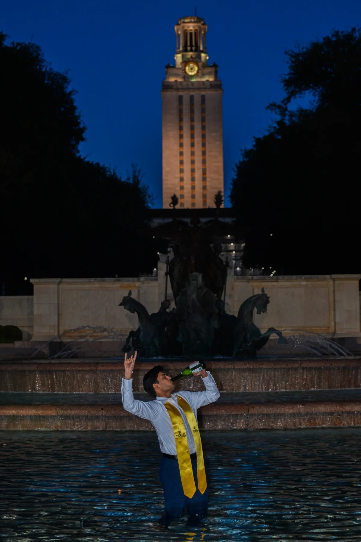 Graduate raising their arms beneath an illuminated tower at night