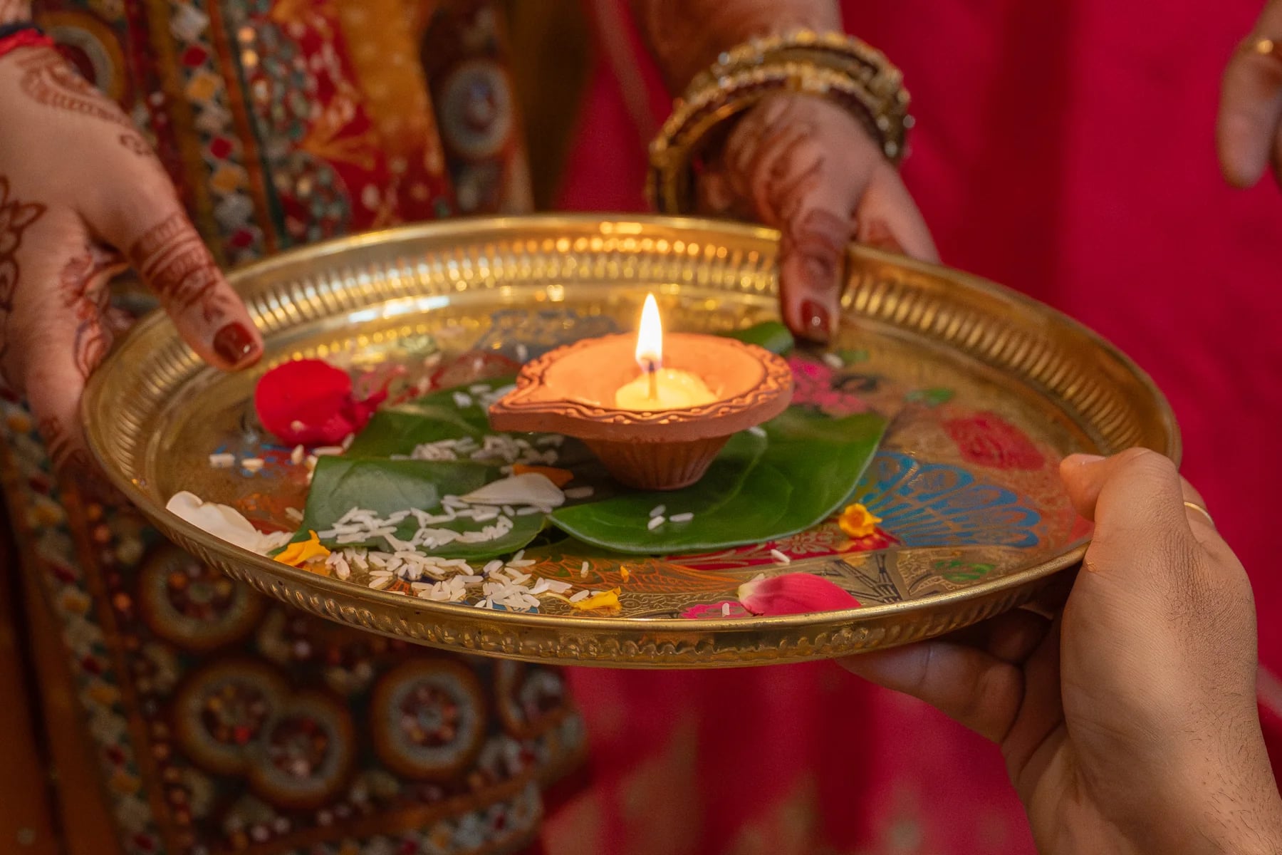 Hands holding a decorated tray with a small flame and flower petals