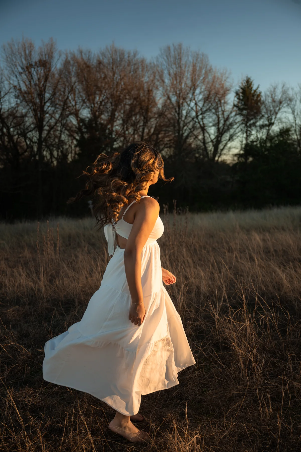 A person turning in a white dress at the edge of a field