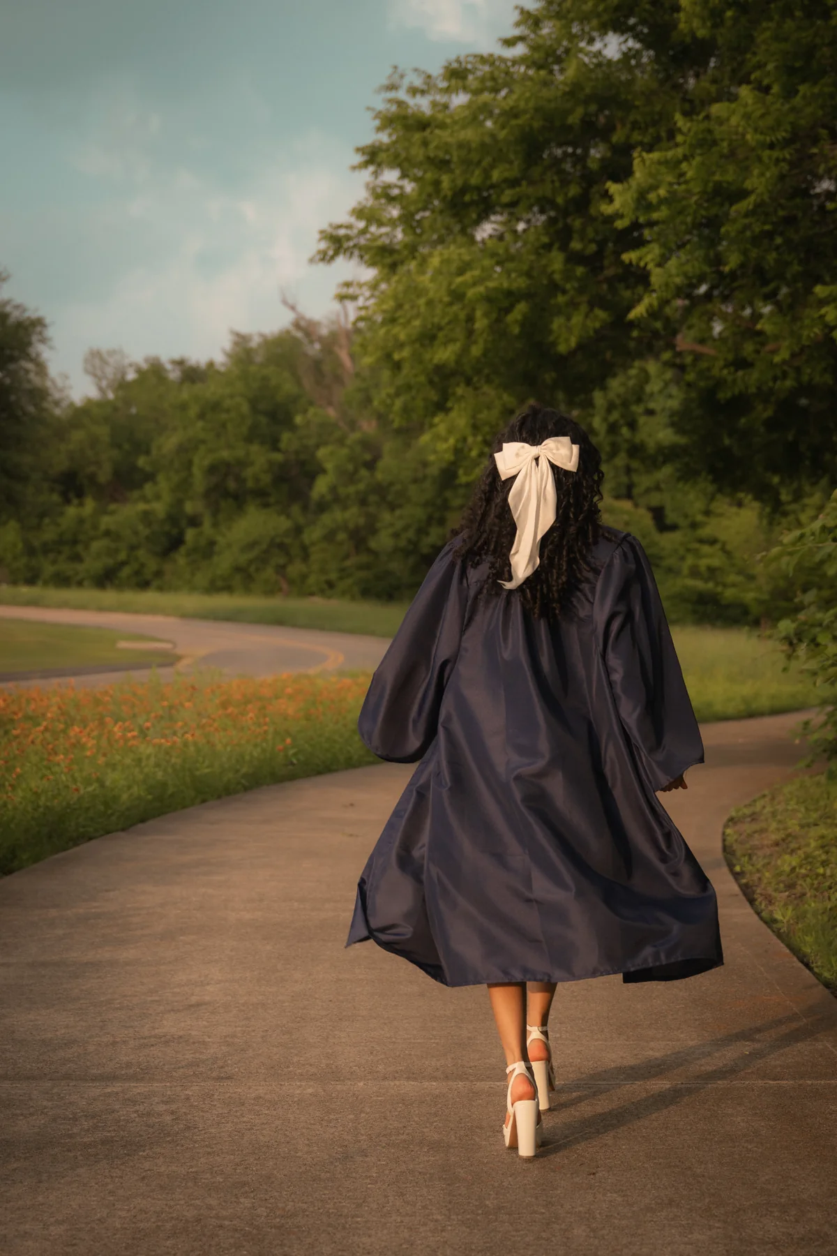 A person in a graduation gown turning on a tree-lined road