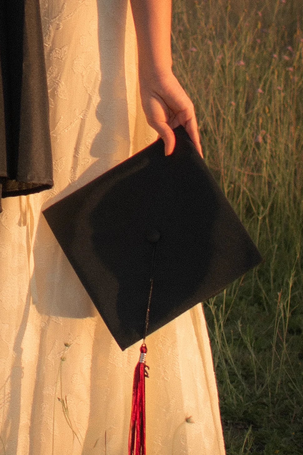 A graduation cap held at the side of a white dress