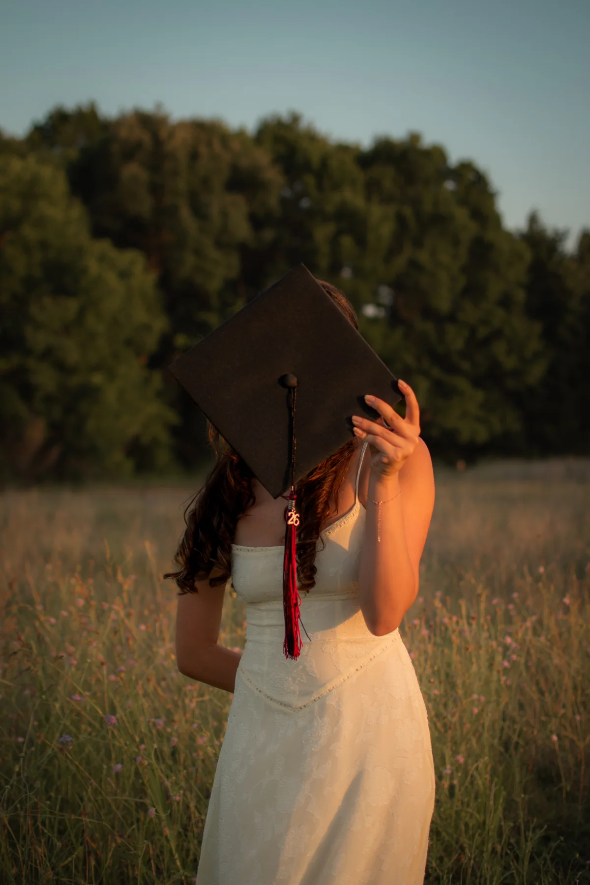 Graduate holding a cap in front of their face in a sunlit field