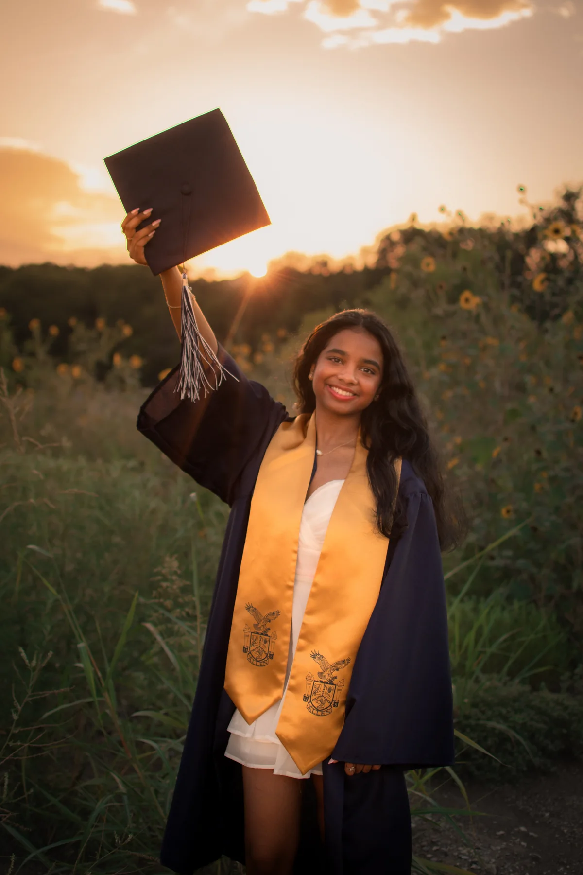 Graduate holding a cap aloft in warm sunset light