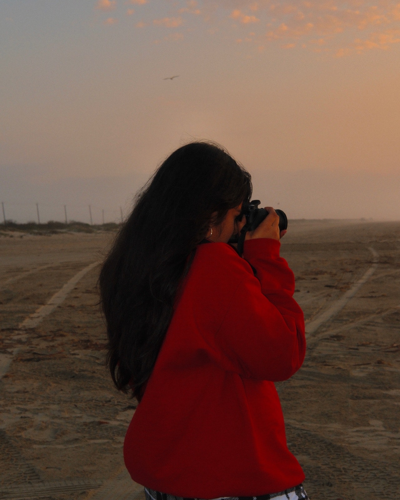 Saanavi taking a photograph on the beach in a red coat